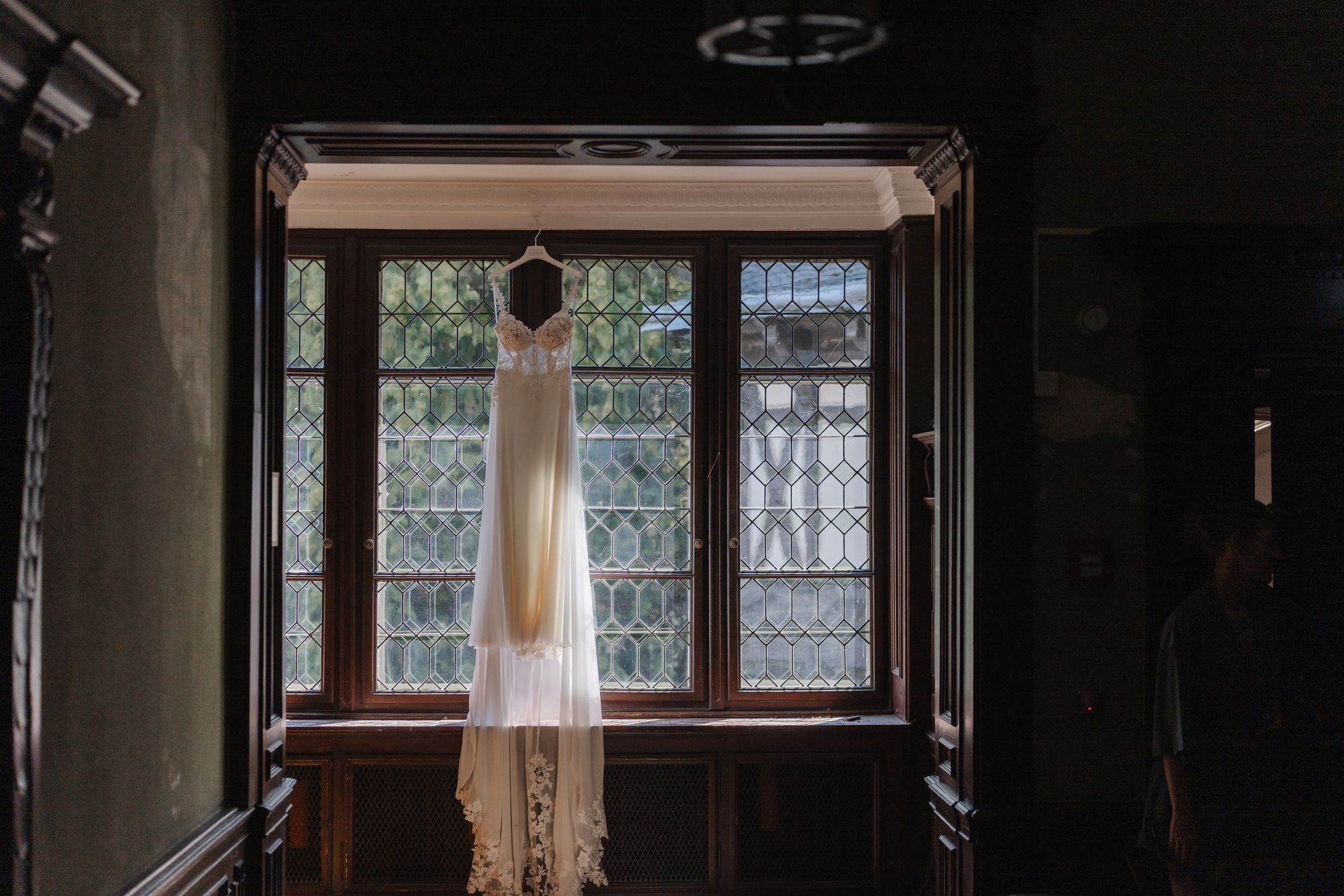 Wedding dress hanging at a leaded glass window in the getting ready suite