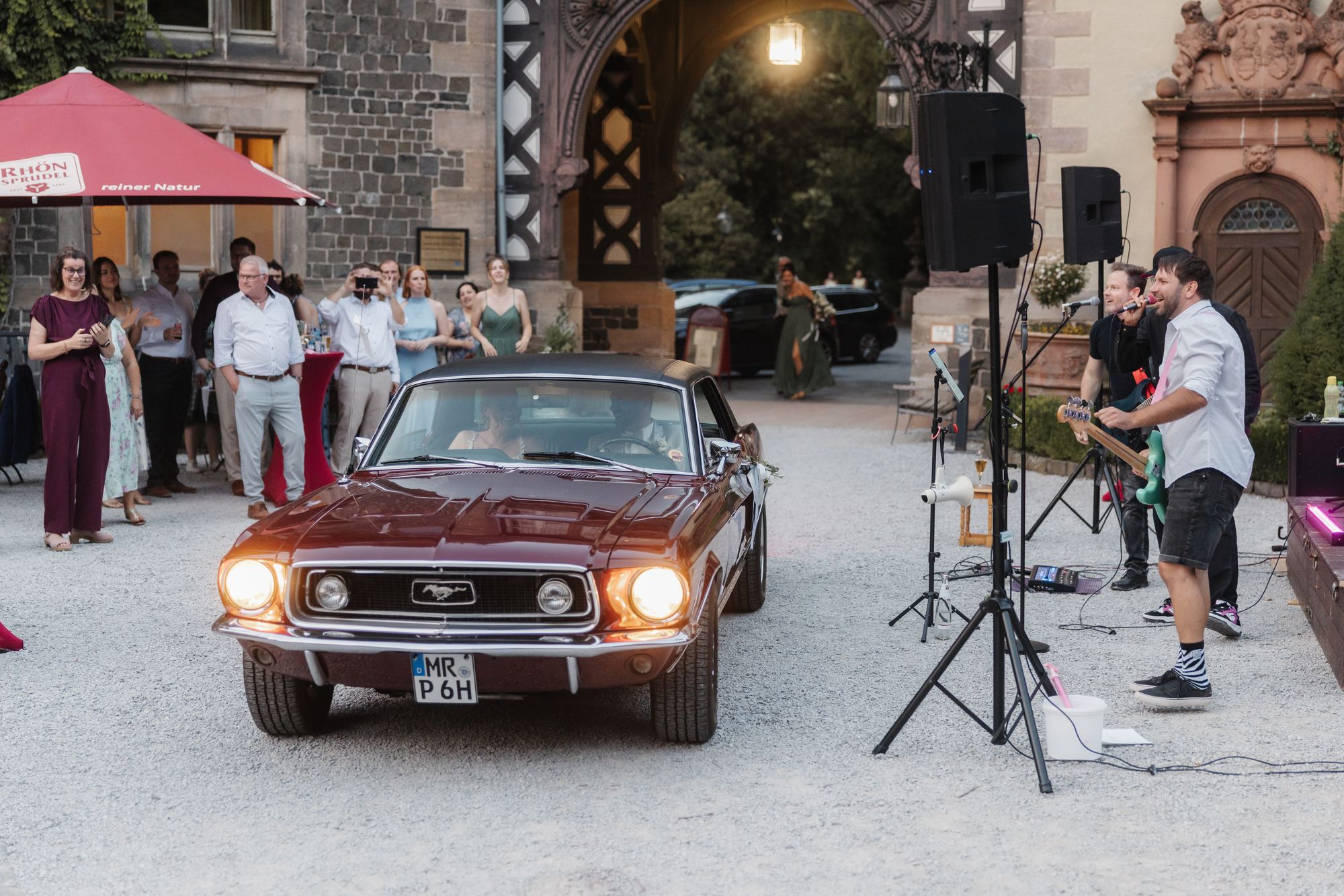Couple arriving in a red Mustang in the courtyard where the surprise band is playing