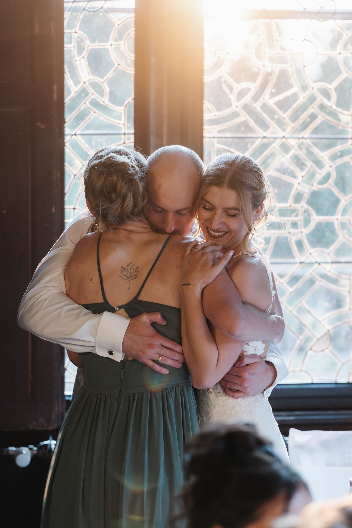 Bride hugging guests in front of a leaded glass window