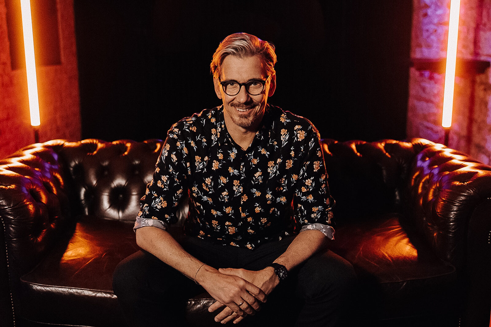 Alex Maus, DJ und Fotograf, auf einem Ledersofa im Neonlicht